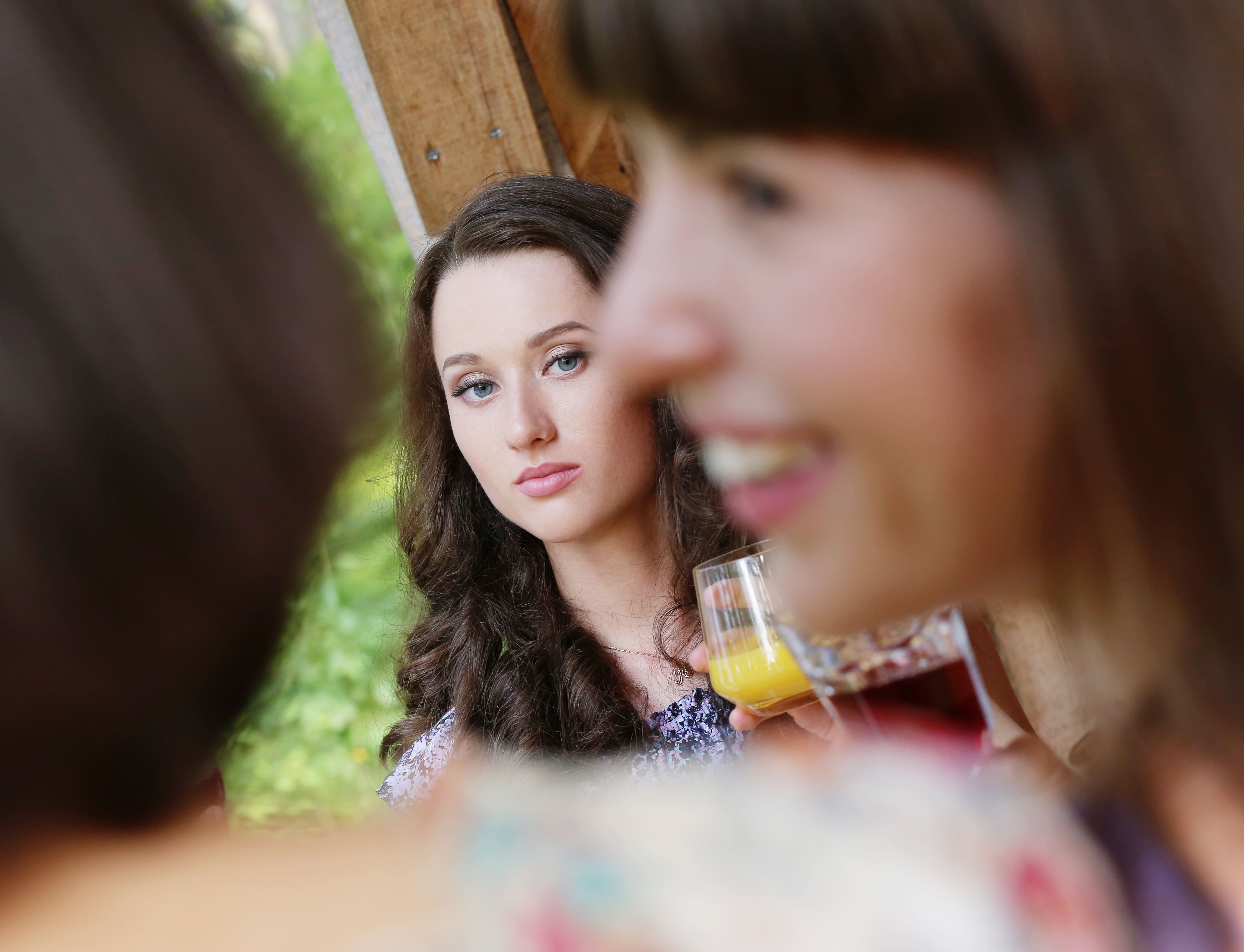 A thoughtful young woman gazes into the distance while in conversation with friends at an outdoor gathering.