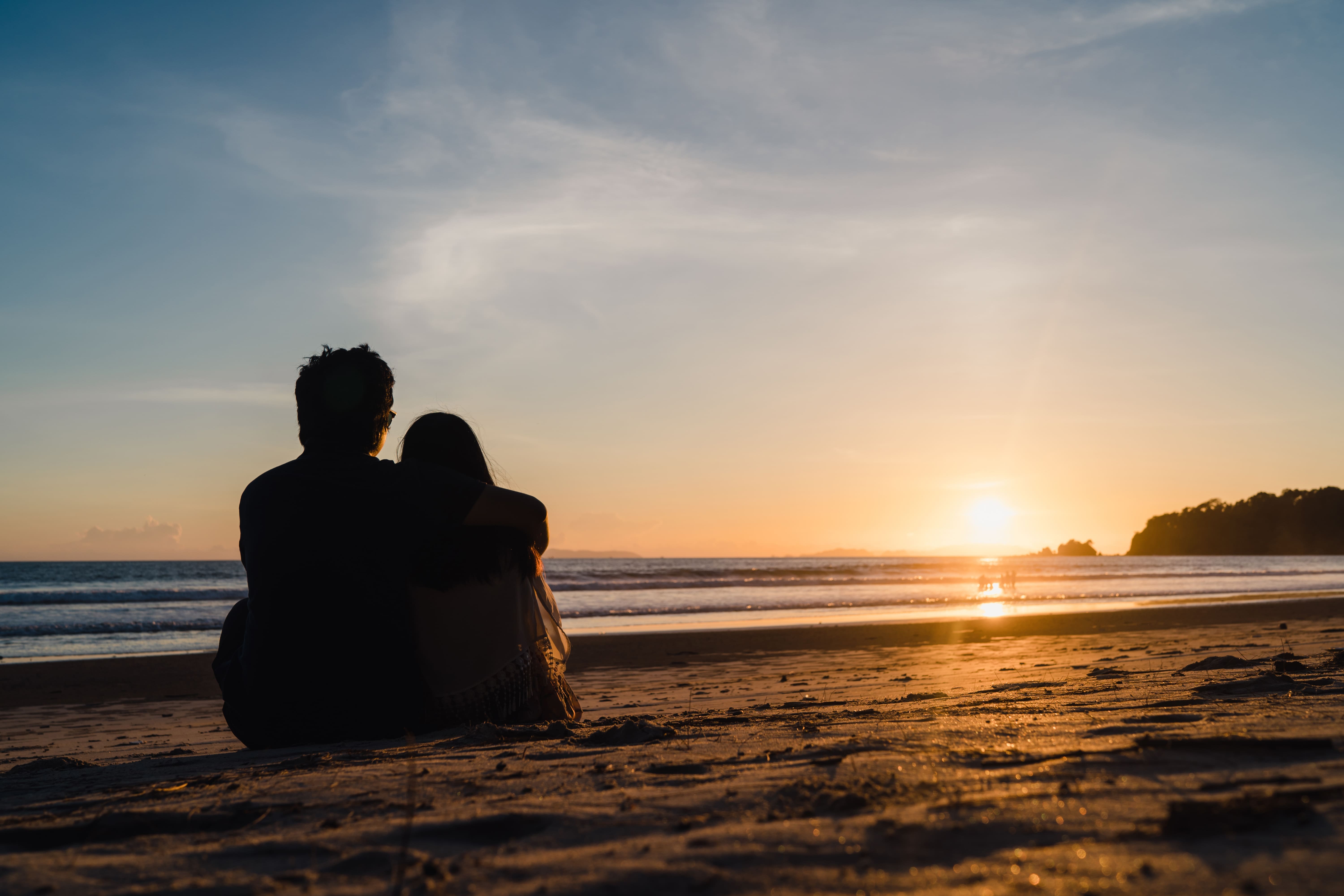 Two people sitting closely together on a beach, enjoying a tranquil sunset over the ocean.